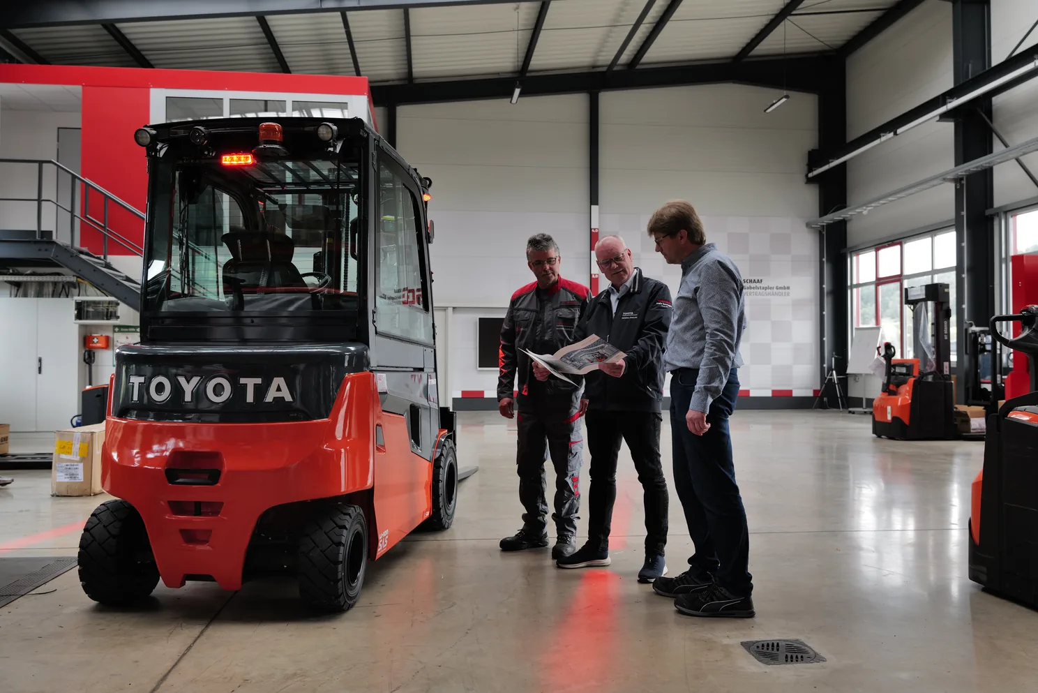 Persönliche Beratung in der Schaaf-Halle: drei Männer besprechen einen Prospekt neben einem Toyota-Elektrostapler